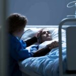 Patient in hospital bed with visitor holding their hand