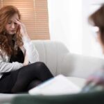Woman with hand on forehead sitting on couch during therapy session
