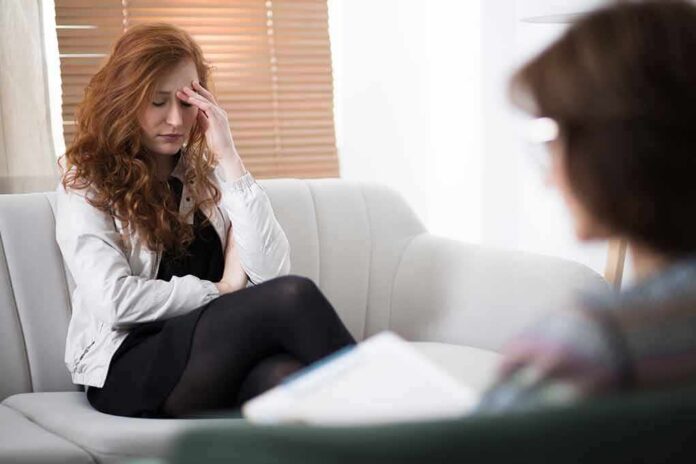 shutterstock_1077356072 Woman with hand on forehead sitting on couch during therapy session