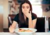 Woman covering mouth while looking at a plate of pasta