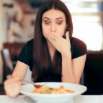 Woman covering mouth while looking at a plate of pasta