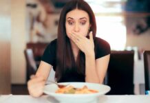 Woman covering mouth while looking at a plate of pasta