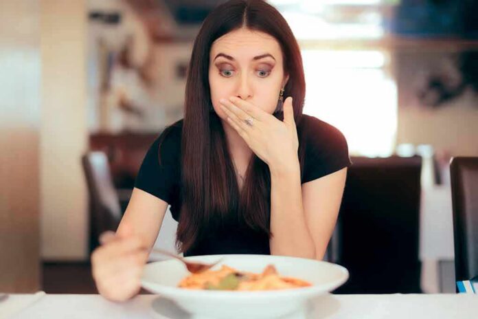 Woman covering mouth while looking at a plate of pasta