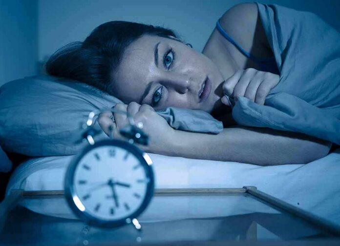 Woman lying awake in bed beside an alarm clock