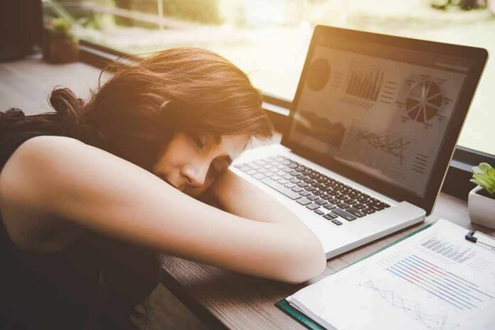 Woman resting her head on desk beside an open laptop