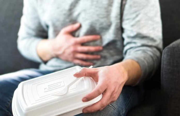 shutterstock_1044903553 Person holding stomach with takeout container on lap