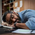 man sleeping at desk with head on arms