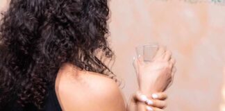Person with curly hair holding a glass and wrist
