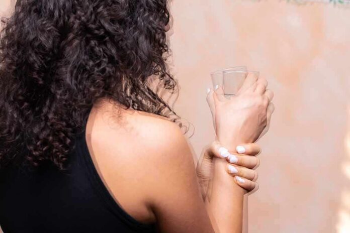 Person with curly hair holding a glass and wrist