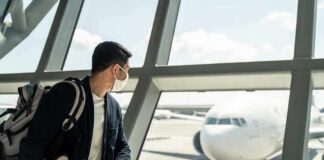 Traveler wearing a mask looks at airplane through airport window