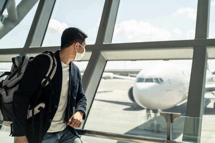 Traveler wearing a mask looks at airplane through airport window