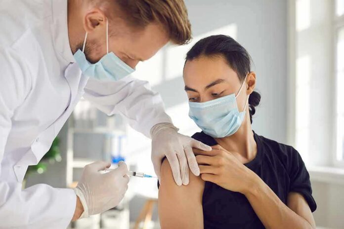 Healthcare worker giving a masked patient a vaccine in the upper arm
