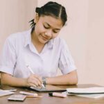 Student writing at a desk with school supplies