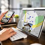 Person using phone and laptop with real estate map app