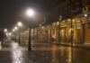 Foggy street with lit lampposts and decorated storefronts at night