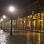 Foggy street with lit lampposts and decorated storefronts at night
