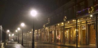 Foggy street with lit lampposts and decorated storefronts at night