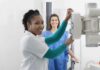 Radiologic technologist adjusting X-ray machine with patient standing behind