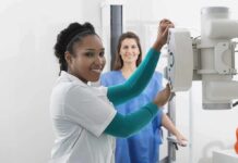 Radiologic technologist adjusting X-ray machine with patient standing behind