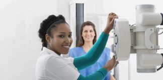 Radiologic technologist adjusting X-ray machine with patient standing behind
