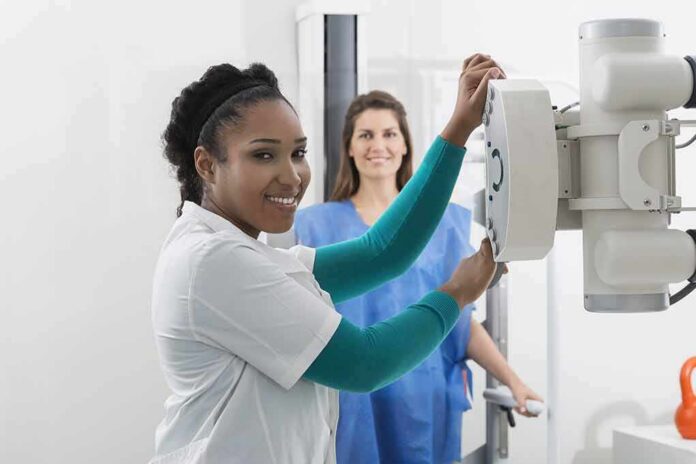 Radiologic technologist adjusting X-ray machine with patient standing behind