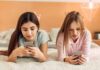 Two girls lying on a bed using smartphones