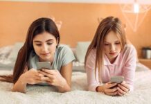 Two girls lying on a bed using smartphones