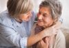 Two older women share a warm embrace on a couch