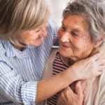 Two older women share a warm embrace on a couch