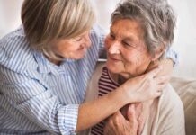 Two older women share a warm embrace on a couch