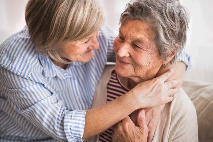 Two older women share a warm embrace on a couch