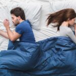 Couple sleeping back to back under a blue blanket