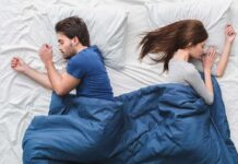 How sleep position affects your heart and brain health Couple sleeping back to back under a blue blanket
