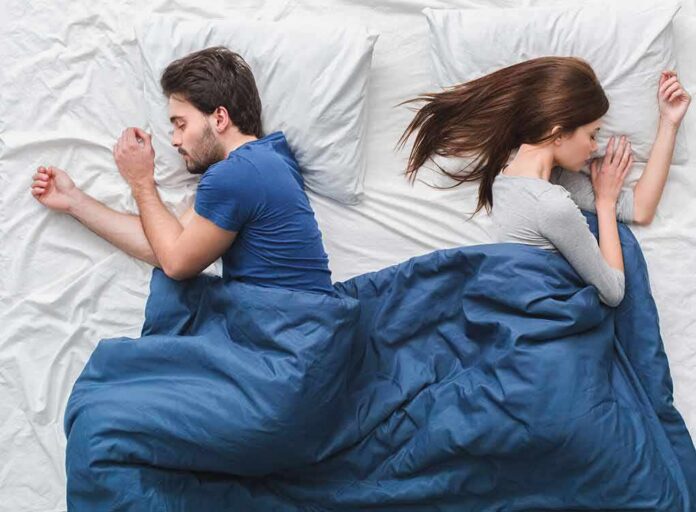 shutterstock_1036490839 Couple sleeping back to back under a blue blanket