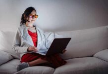 Why Some People Become Night Owls Naturally Person wearing orange glasses using a laptop on a white couch