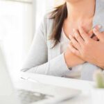 person clutching chest with both hands at a desk