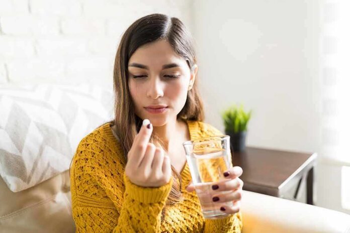 shutterstock_1287312472 Woman holding a pill and a glass of water