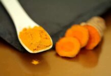Turmeric powder on a white spoon beside sliced turmeric root