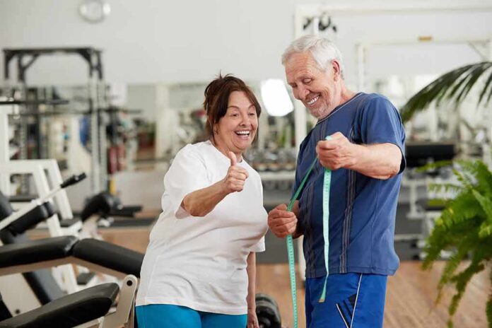 Older man and woman smiling with measuring tape in a gym