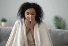 FLU-COVID-RSV: Johns Hopkins Drops Cold-Season Playbook Woman wrapped in a blanket blowing her nose