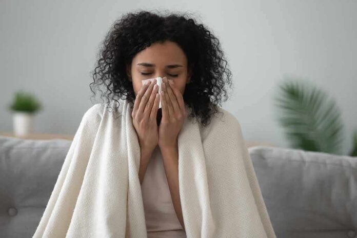 Woman wrapped in a blanket blowing her nose