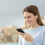 Woman with wireless earbuds using a smartphone outdoors