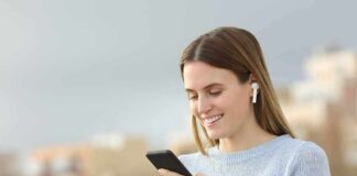 Woman with wireless earbuds using a smartphone outdoors