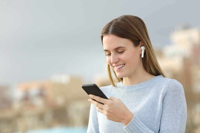 Woman with wireless earbuds using a smartphone outdoors