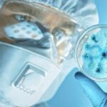 Scientist in protective gear examining a petri dish