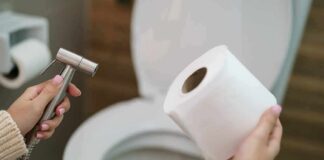 Hands holding a bidet sprayer and toilet paper near an open toilet