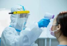 Why do you get a fever when you’re sick? Healthcare worker in PPE checks patient temperature with infrared thermometer