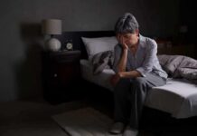Older adult sitting on bed with head in hand