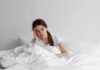 Morning Brain Fog? Here’s The Sneaky Culprit Woman sitting in bed looking tired with hand on head