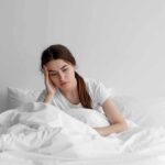 Woman sitting in bed looking tired with hand on head